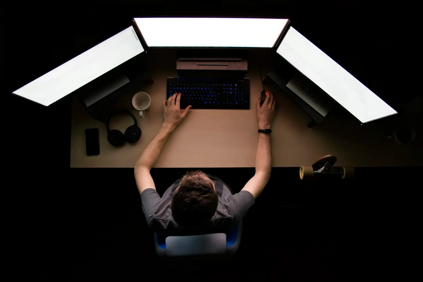 An engineer at a desk lit by three screens, seen from above.