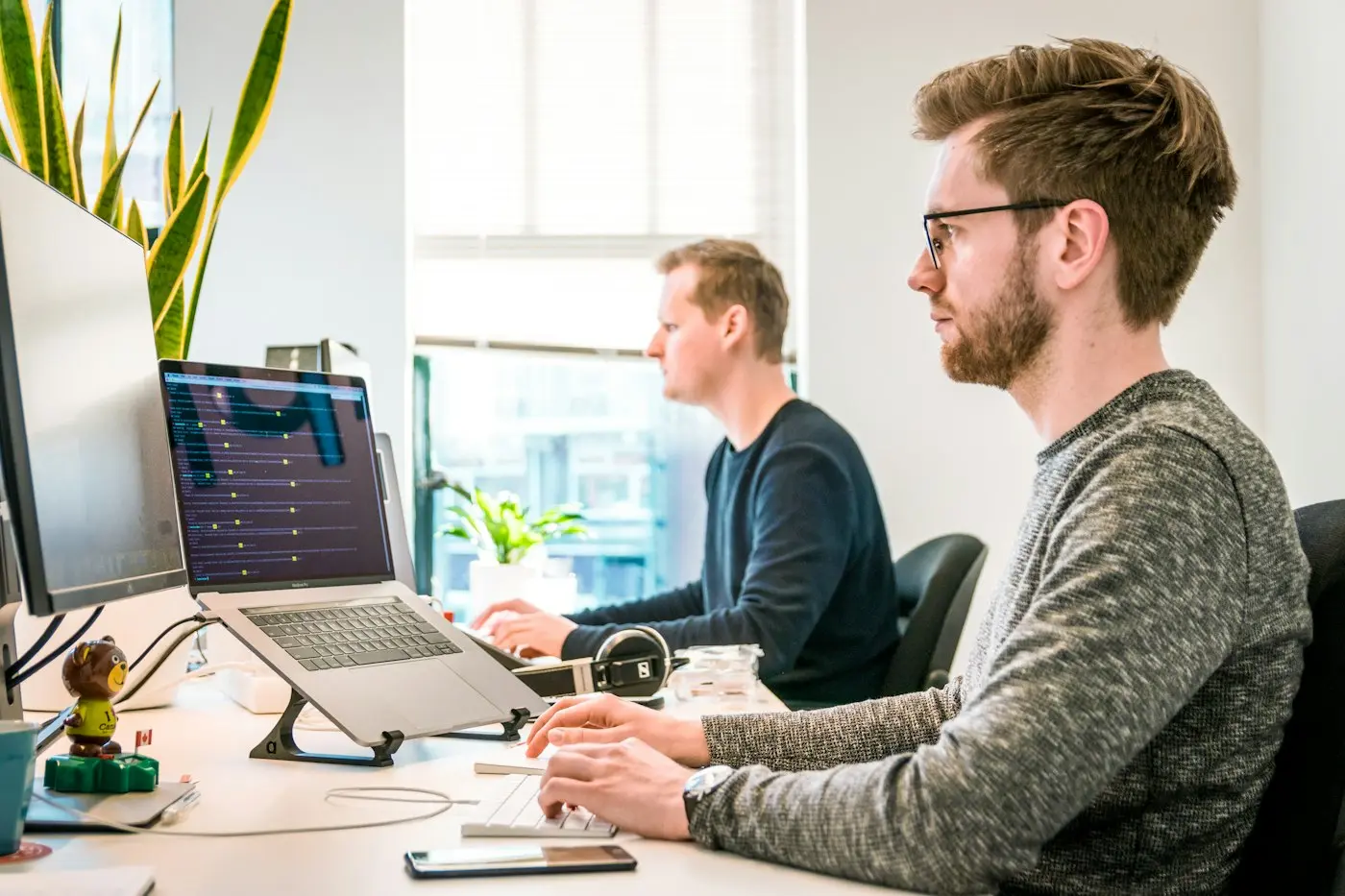 Two engineers at their desks with code on large monitors.