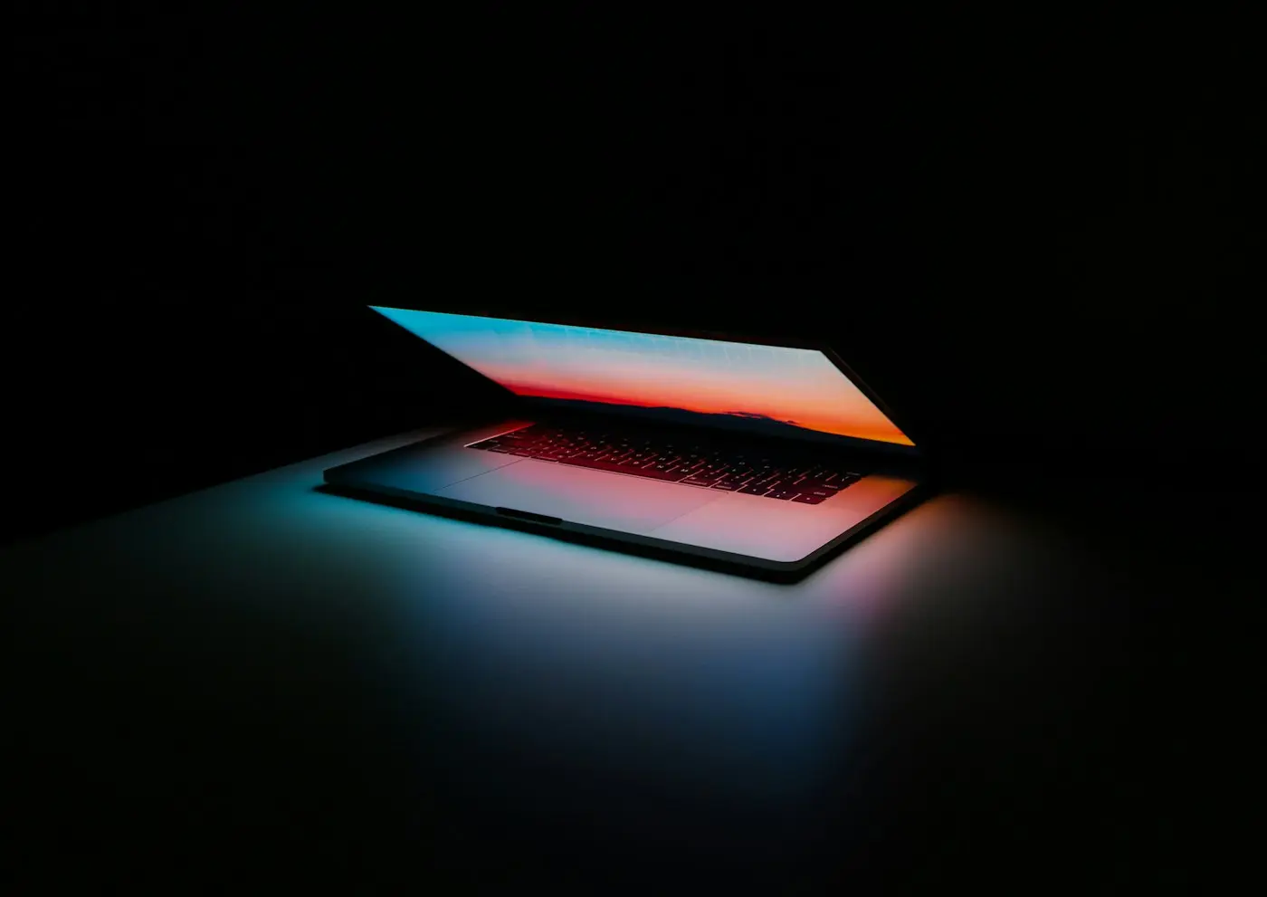 A laptop opening in the dark, its screen glowing.