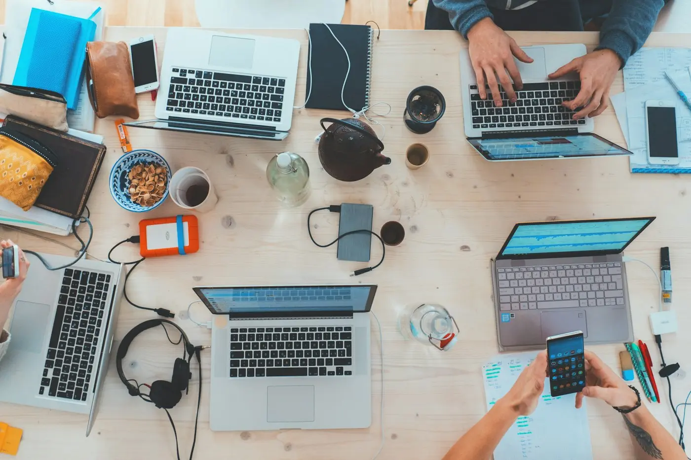 Laptops, notebooks and coffee on a shared desk, seen from above.