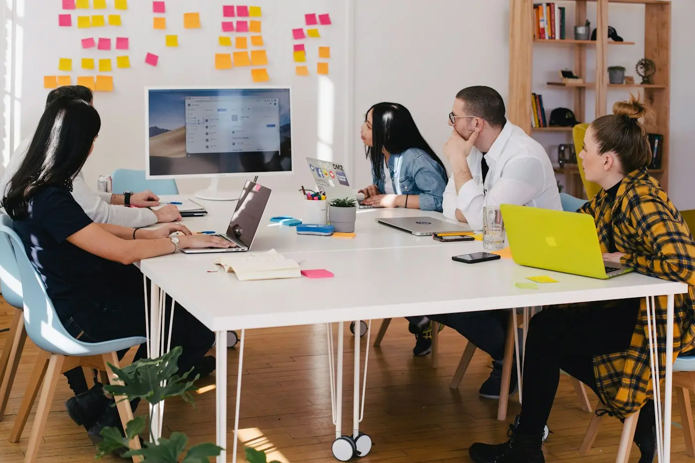 A team around a workshop table, a wall of notes behind them.